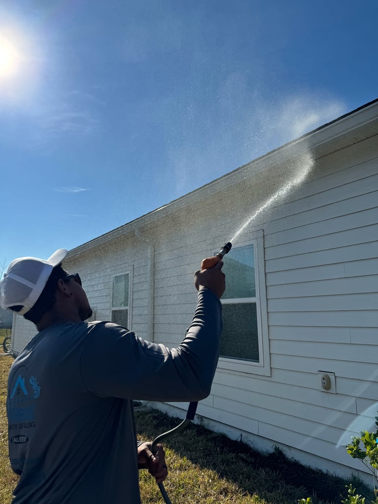 Worker pressure washing the exterior wall of a white mobile home on a sunny day